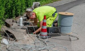Broadband infrastructure roadside installation - ALTA SURVEY North Carolina A construction worker installs underground broadband cables near a roadside drain, showing how infrastructure rebuilds connect to stormwater design