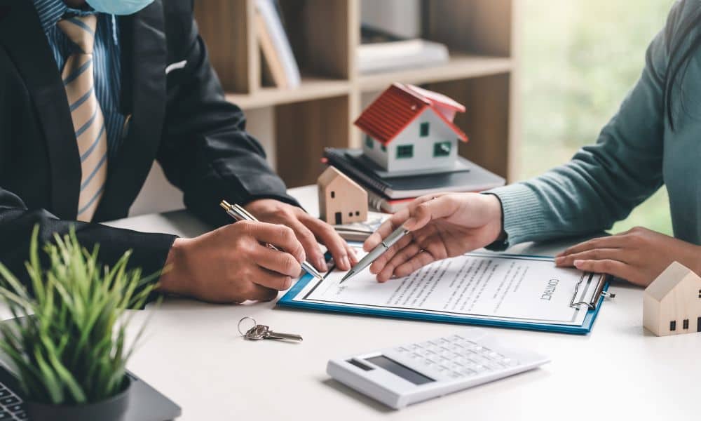 Homebuyers signing real estate documents with house models and keys on the table, representing the importance of an elevation certificate for property closings