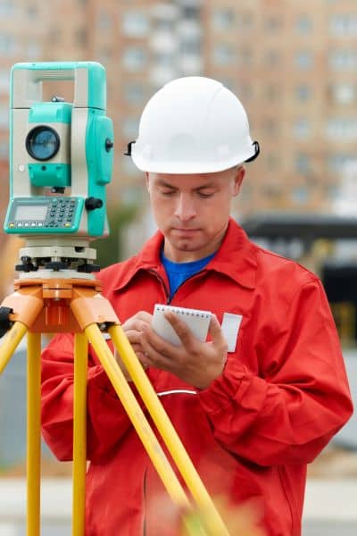 Licensed land surveyor measuring property elevation for FEMA elevation certificate.