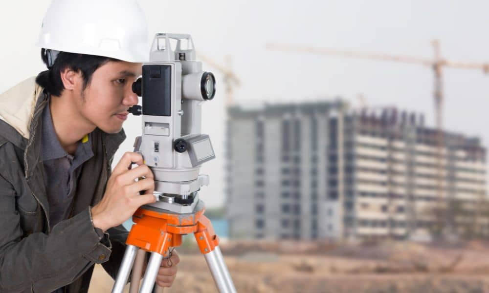 A land surveyor using a total station to check site conditions before construction