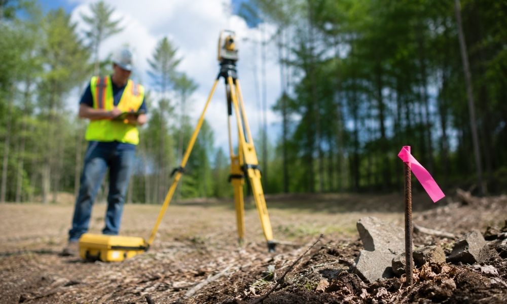 Surveyor locating a missing property corner marker, a common issue that can affect land survey cost