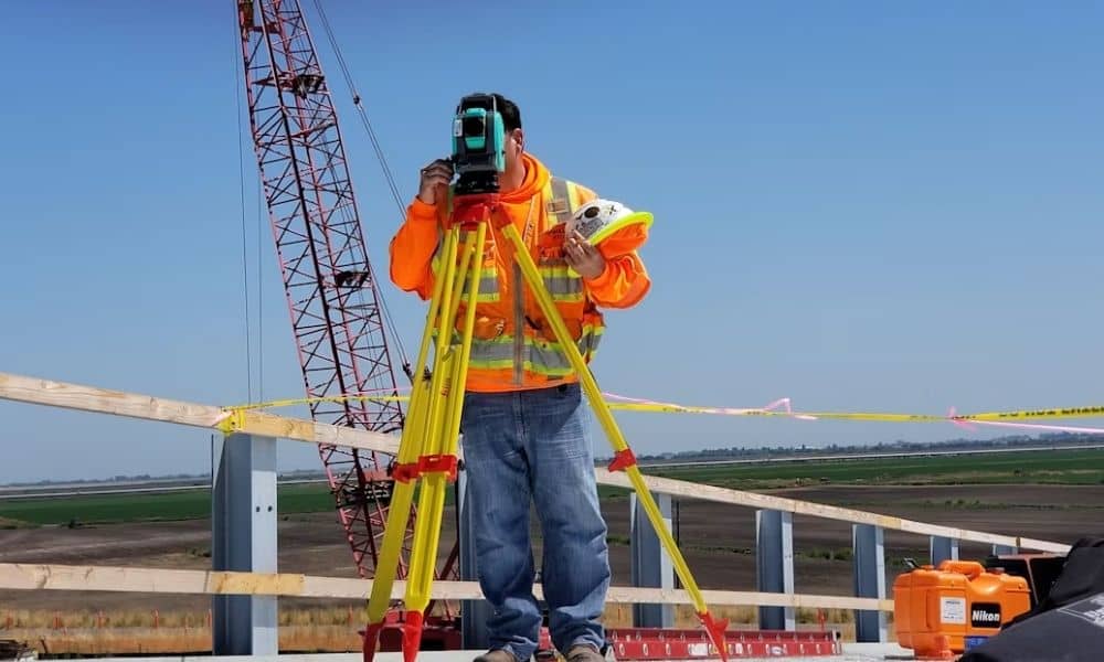 Surveyor operating a total station at a construction site, with equipment used for elevation surveys